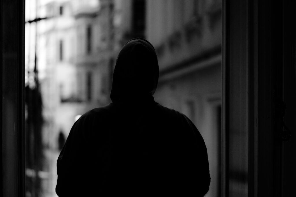 Black and white image of a hooded figure in an urban environment, creating a mysterious silhouette.