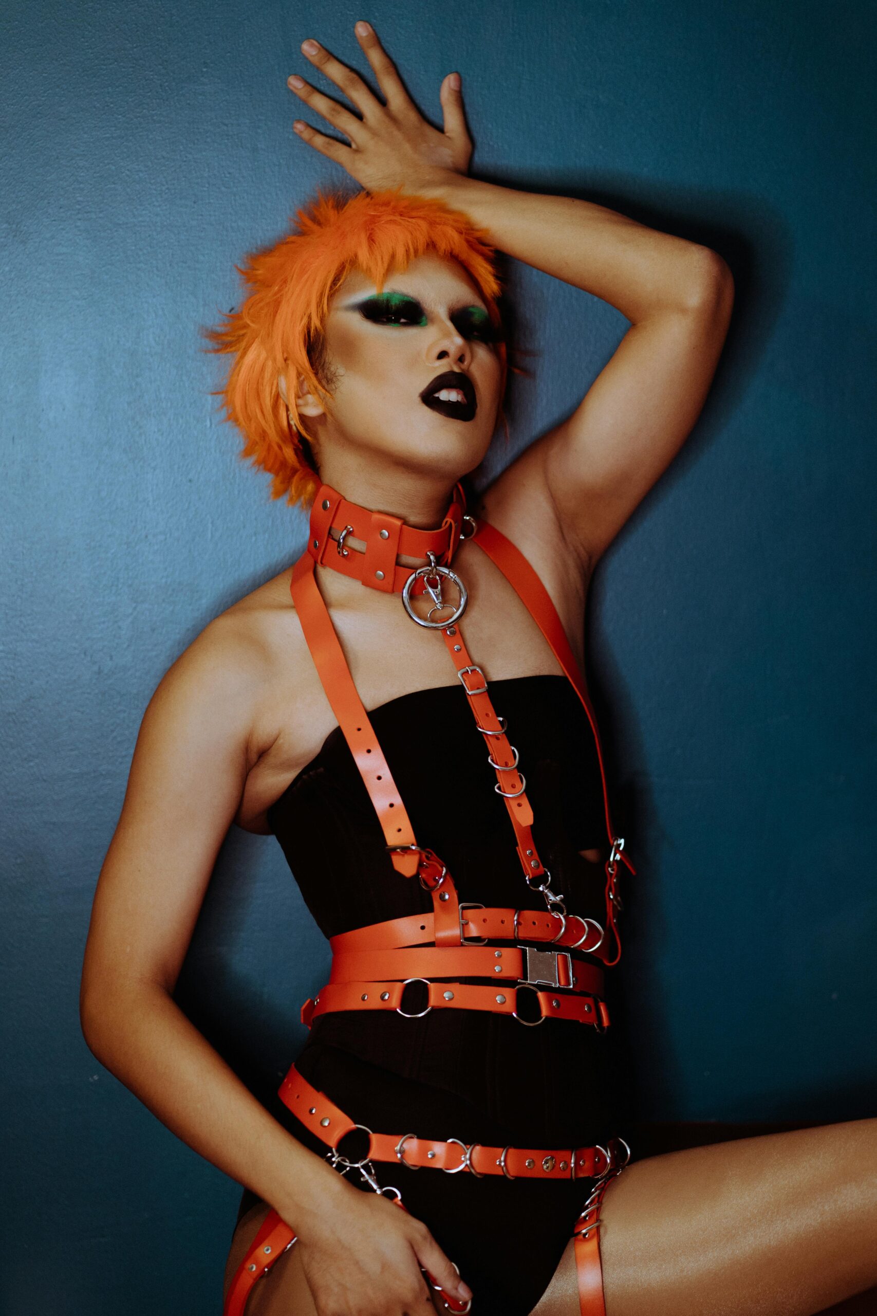 Model posing in avant-garde attire with vibrant makeup and striking orange wig.